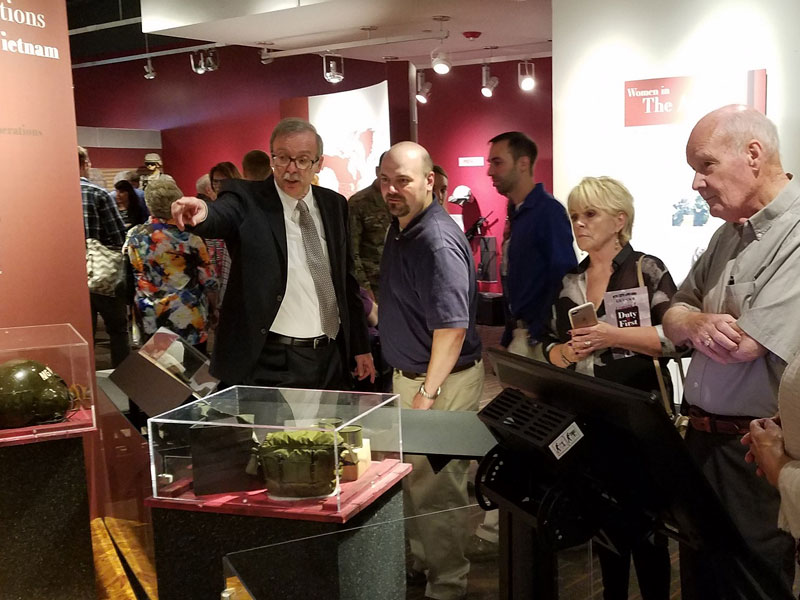 Several people standing and observing museum exhibits in crowded room